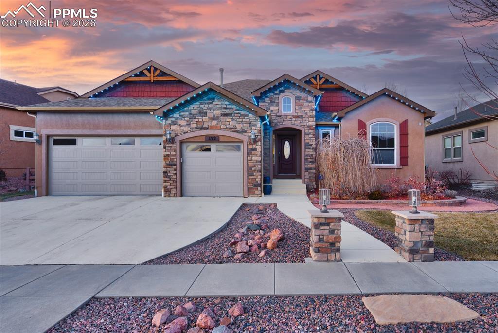 View of front of home featuring concrete driveway, stone siding, a garage, and stucco siding