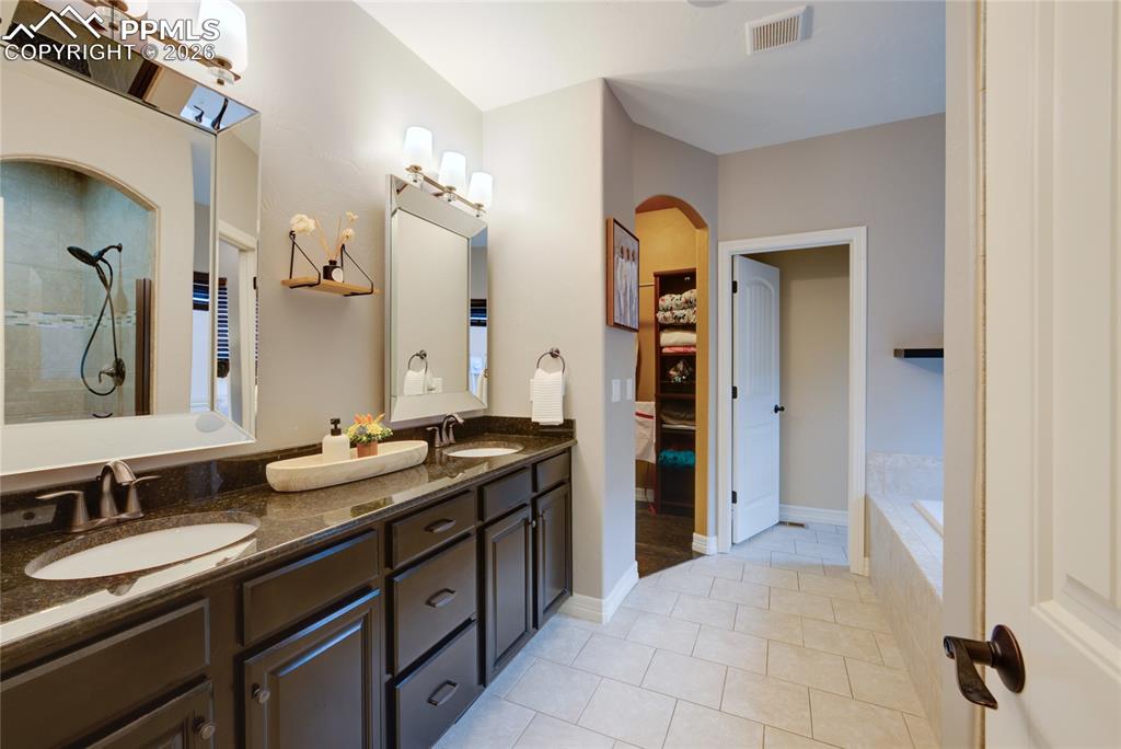 1112 Spectrum Loop Colorado Springs, CO 80921 - Photo 11 of 50 Full bath with double vanity, light tile patterned flooring, a relaxing tiled tub, and a shower