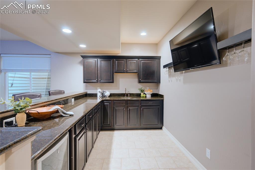 1112 Spectrum Loop Colorado Springs, CO 80921 - Photo 28 of 50 Kitchen featuring dark stone counters, wine cooler, dark brown cabinetry, recessed lighting, and light tile patterned flooring