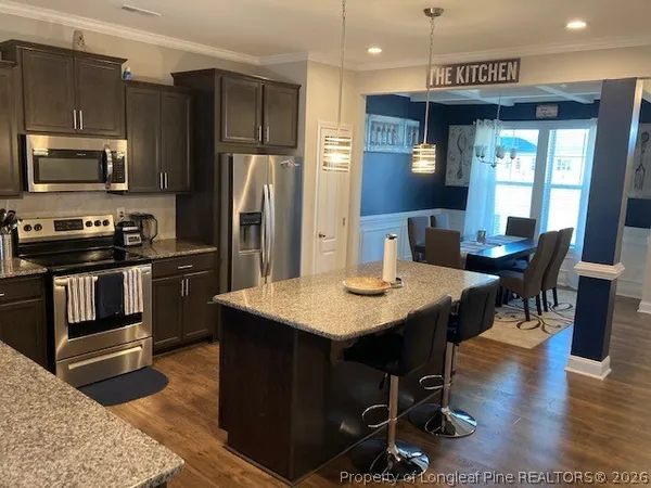 a kitchen with stainless steel appliances kitchen island granite countertop a stove a refrigerator a sink a dining table and chairs with wooden floor