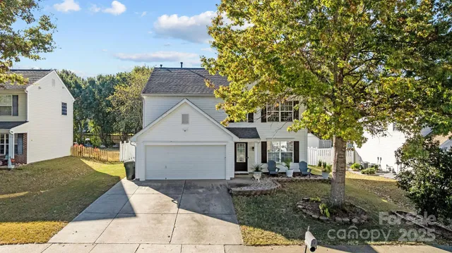 a view of a white house next to a yard with plants and trees