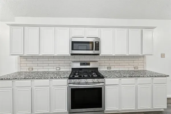 a kitchen with granite countertop white cabinets and stainless steel appliances