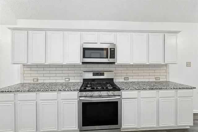 a kitchen with granite countertop white cabinets and stainless steel appliances