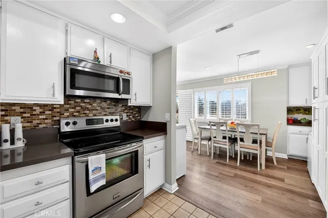 a kitchen with stainless steel appliances a stove a sink a microwave a dining table and chairs with wooden floor