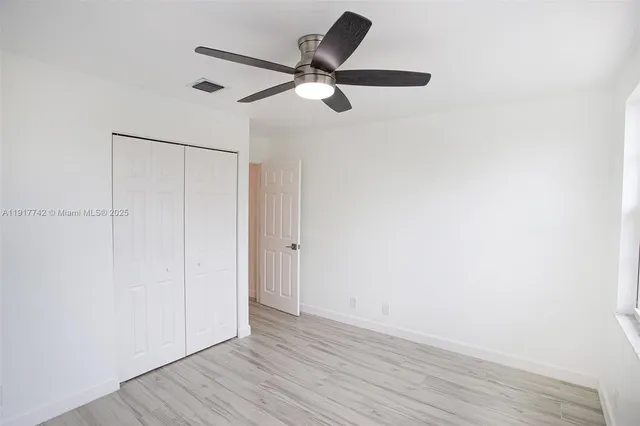 an empty room with wooden floor closet and windows