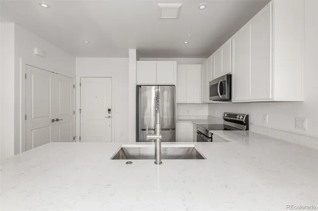 a spacious bedroom with a bed a chandelier a flat screen tv and a refrigerator