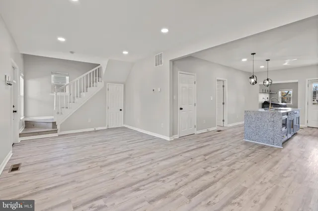 a view of an empty room with wooden floor and a kitchen
