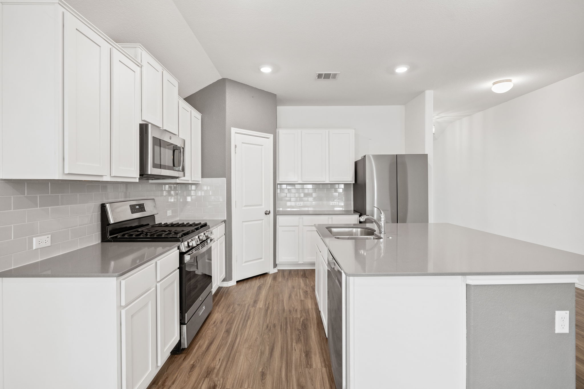 127 George Kimble Cove Bastrop, TX 78602 - Photo 13 of 40 Kitchen featuring appliances with stainless steel finishes, dark wood-type flooring, decorative backsplash, a kitchen island with sink, and white cabinetry