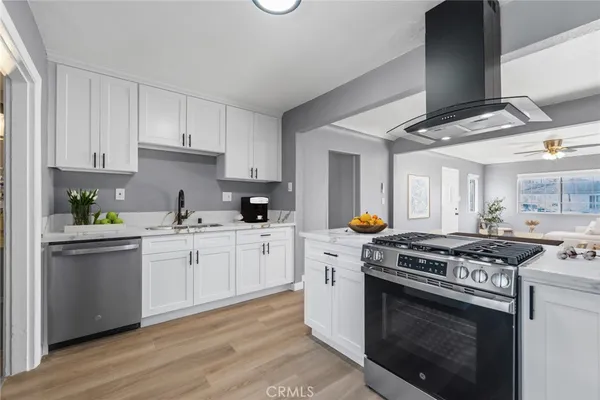 a kitchen with stainless steel appliances granite countertop a stove a sink dishwasher and white cabinets with wooden floor