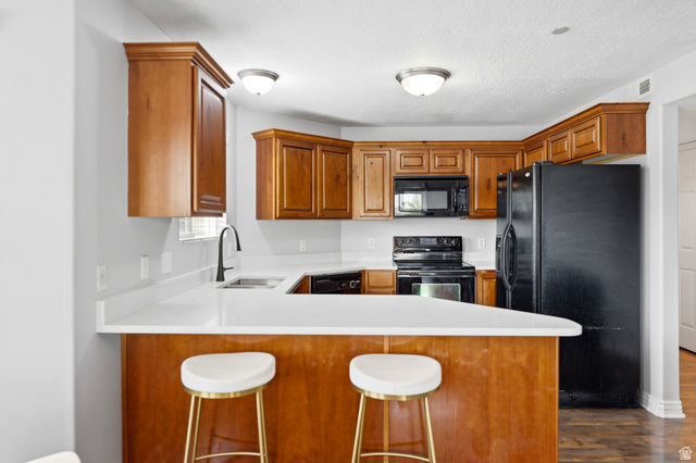 116 East Resaca Drive, Unit F6 Sandy, UT 84070 - Photo 12 of 32 Kitchen featuring wood cabinetry, white countertops, black appliances, and a breakfast bar with seating space
