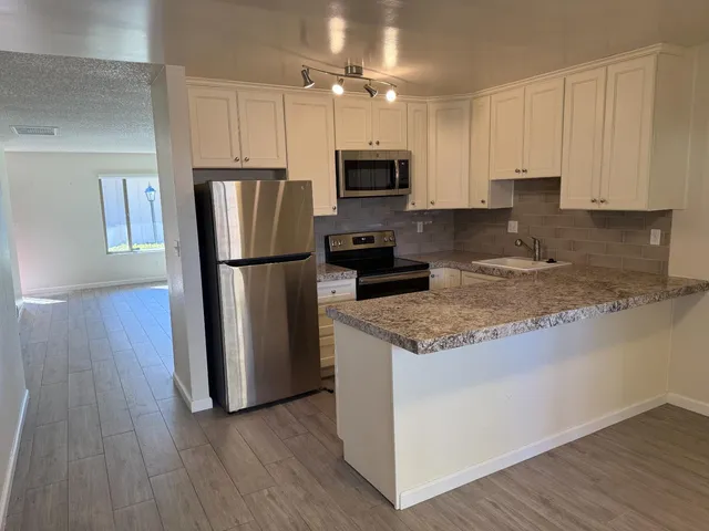 a kitchen with granite countertop a refrigerator a sink a stove a microwave and wooden floor