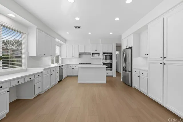 a large kitchen with stainless steel appliances granite countertop a large counter top a sink a refrigerator and a cabinets