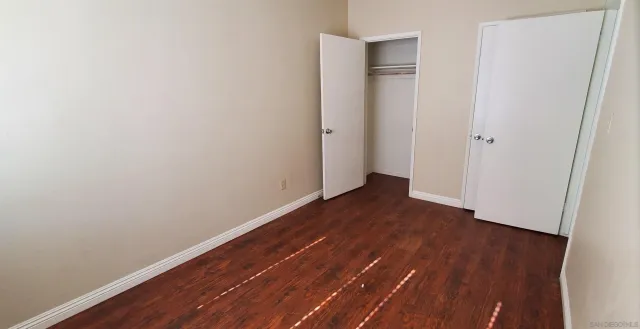 a view of an empty room with wooden floor and closet