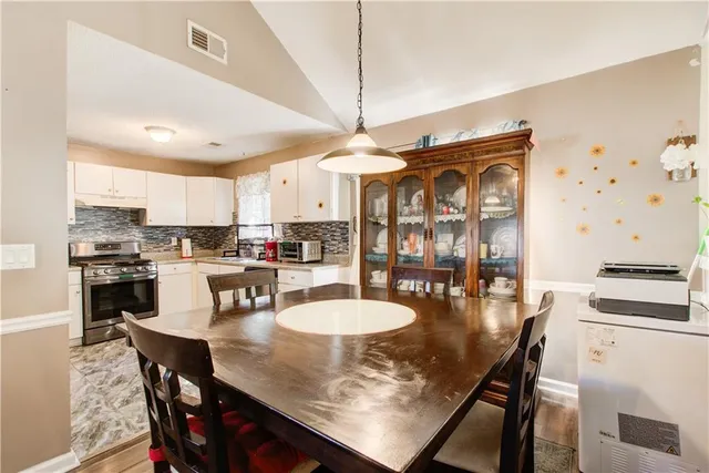 a kitchen with stainless steel appliances granite countertop a stove a refrigerator a kitchen island a dining table and chairs with wooden floor