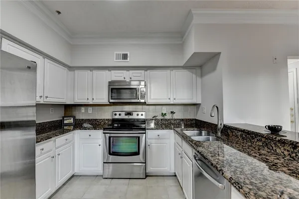 a kitchen with stainless steel appliances granite countertop white cabinets a sink a stove and a refrigerator