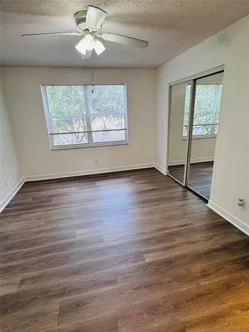an empty room with wooden floor chandelier fan and windows