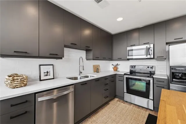 a kitchen with stainless steel appliances granite countertop a sink a stove a refrigerator a microwave with wooden cabinets and floor