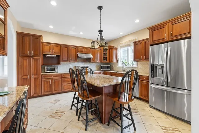 a kitchen with stainless steel appliances granite countertop a refrigerator a stove top oven a sink dishwasher and a dining table with wooden floor