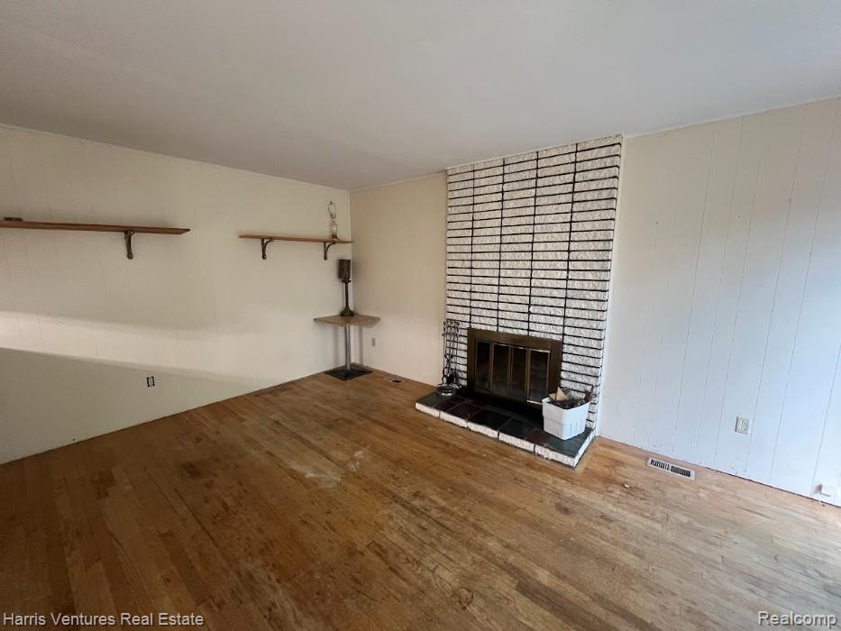 28482 Sutherland Avenue Warren, MI 48088 - Photo 12 of 25 Spacious family room featuring wood-finish flooring, a prominent brick fireplace with a black tile hearth, and ceiling-mounted light fixtures