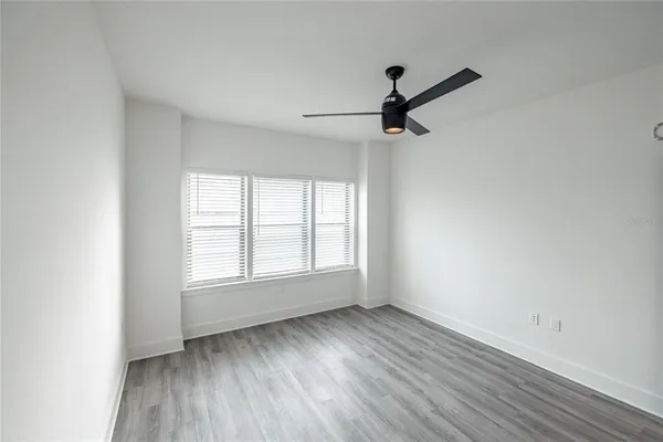 an empty room with wooden floor ceiling fan and windows