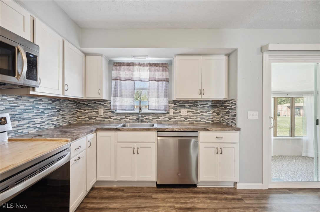 5476 Lear Nagle Road North Ridgeville, OH 44039 - Photo 12 of 38 Kitchen featuring backsplash, dark wood-type flooring, appliances with stainless steel finishes, white cabinets, and a sink