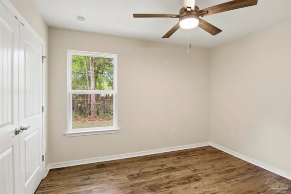 an empty room with wooden floor fan and windows