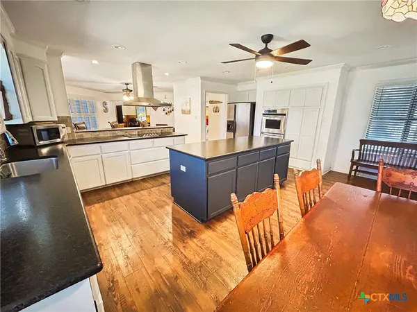 a kitchen with stainless steel appliances kitchen island granite countertop a table chairs in it and a living room view