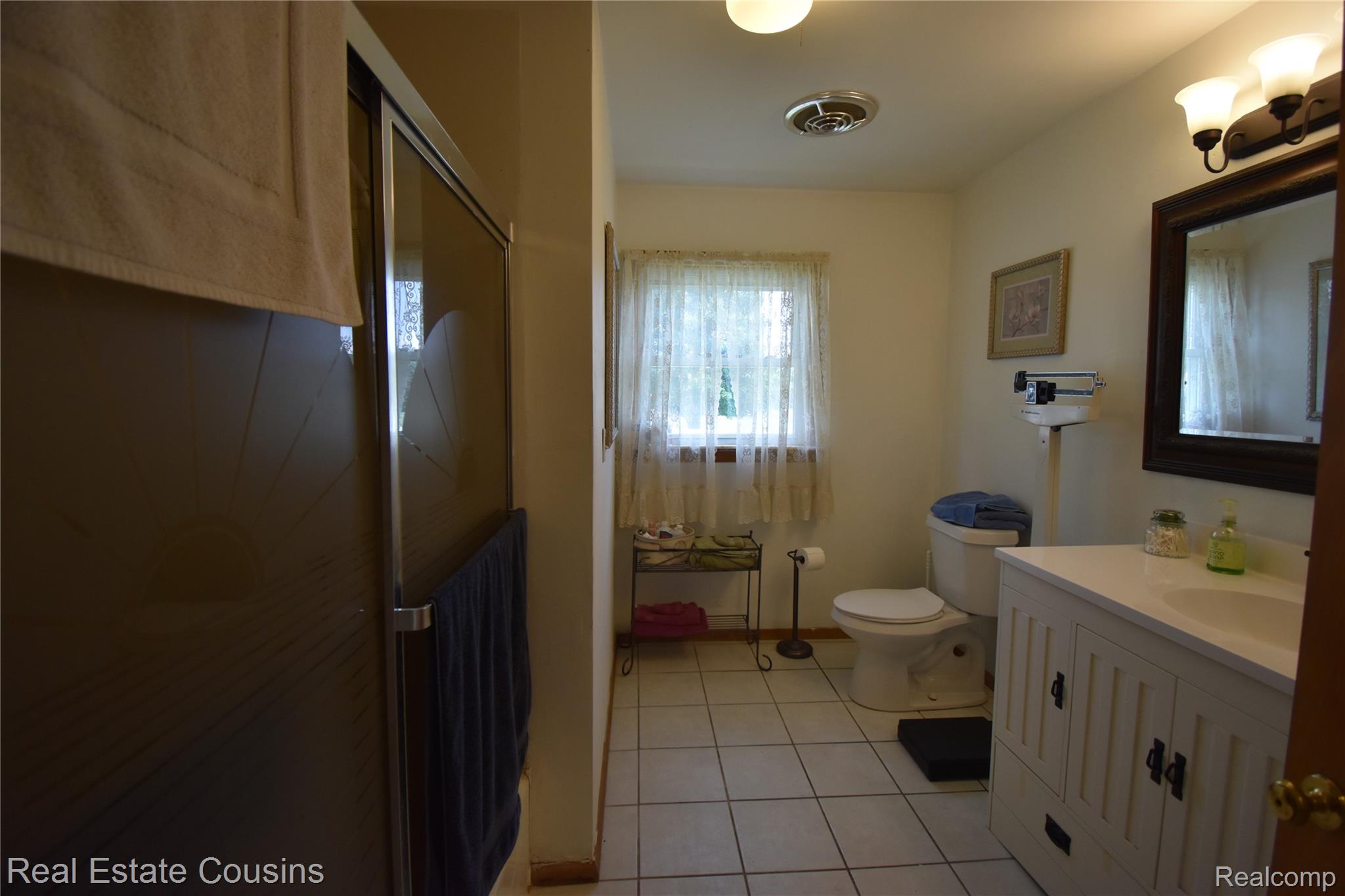 2247 Johnson Mill Road North Branch, MI 48461 - Photo 8 of 22 Bathroom featuring a shower with sliding glass doors, a single window, a commode, a white vanity with a single sink, and a wall-mounted mirror