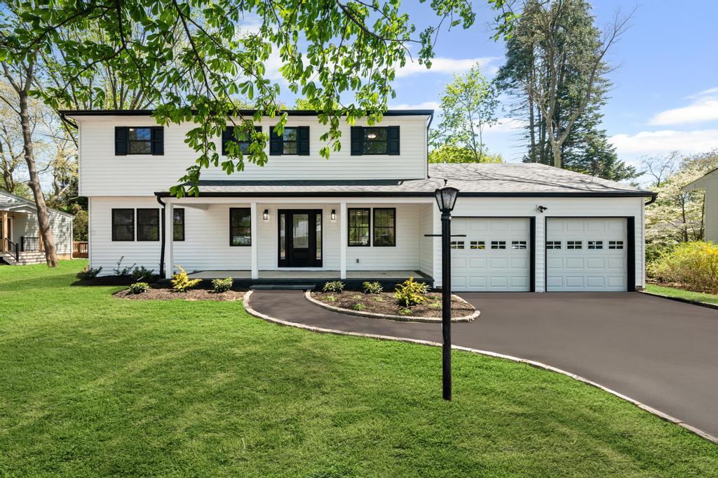 View of front of house with covered porch, an attached garage, driveway, and a front lawn