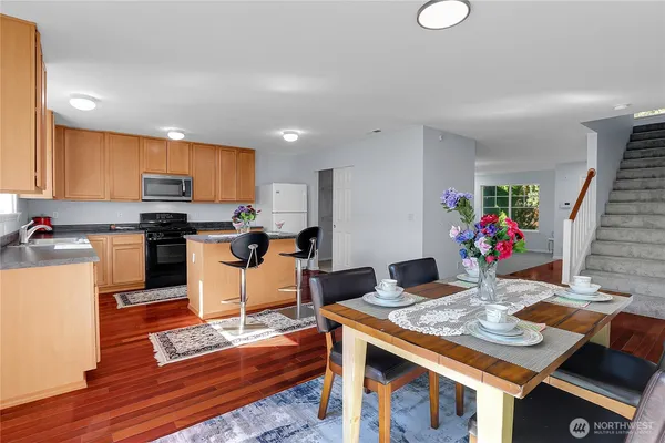 a open kitchen with stainless steel appliances granite countertop a stove top oven a dining table and chairs with wooden floor