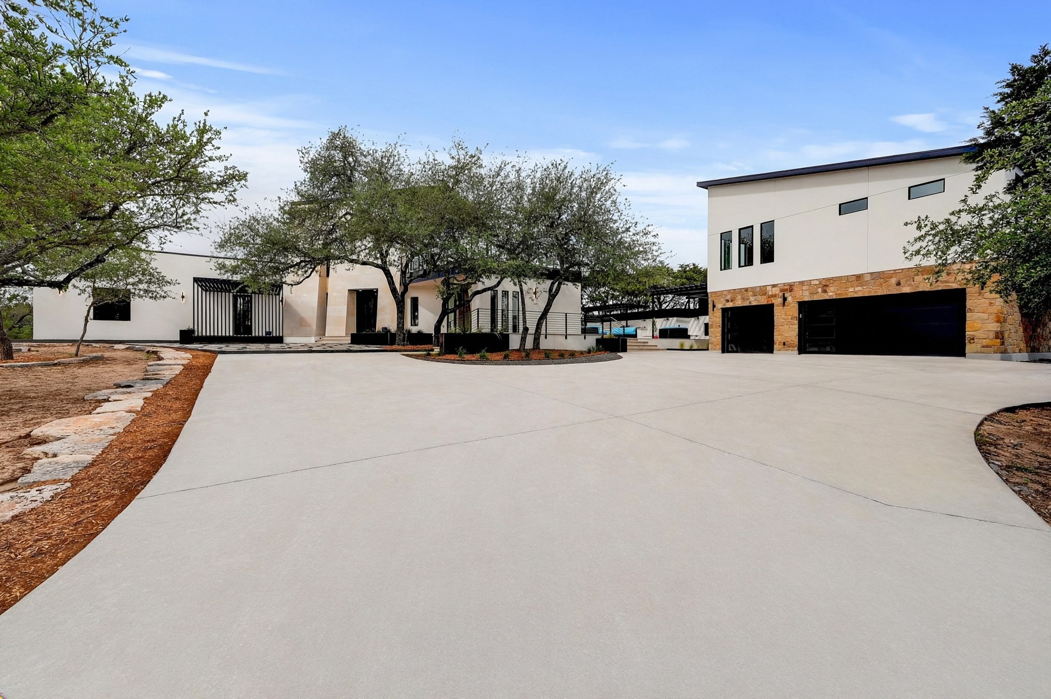 700 Rancho Grande Drive Wimberley, TX 78676 - Photo 3 of 39 The property features an extensive concrete driveway, mature trees, and a modern exterior facade with stone accents