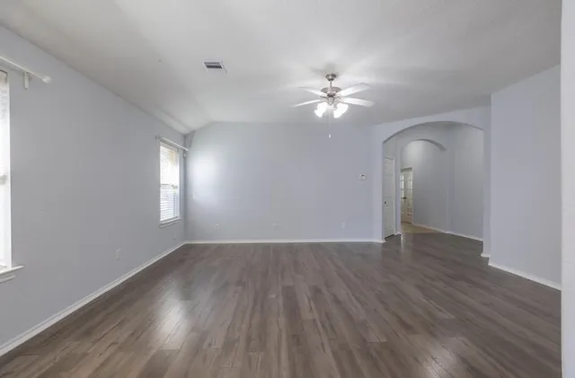 an empty room with wooden floor chandelier fan and windows