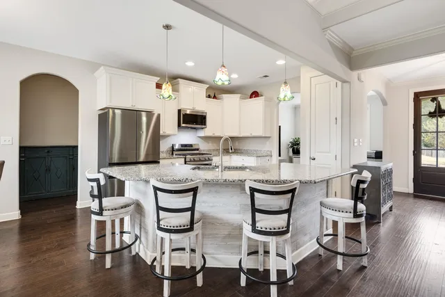 a kitchen with stainless steel appliances kitchen island granite countertop a dining table chairs and a refrigerator