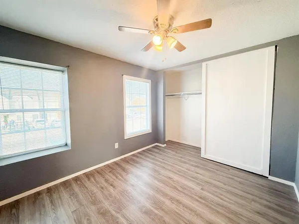 an empty room with wooden floor closet and windows