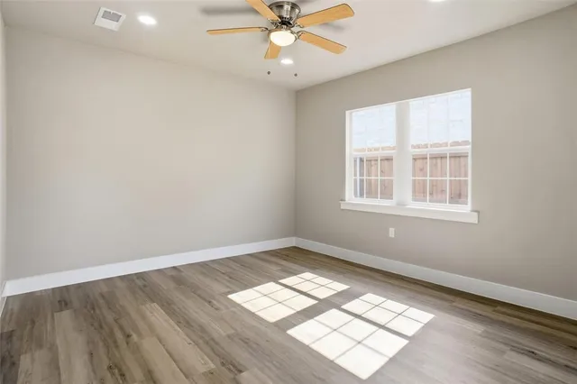 an empty room with wooden floor windows and fan