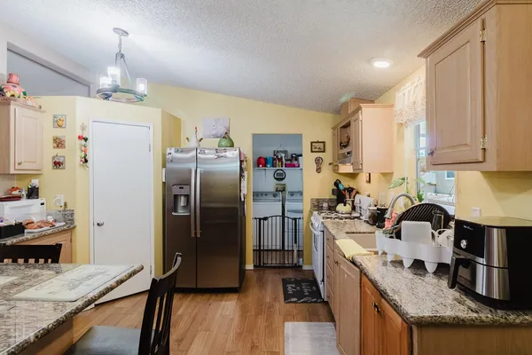 a kitchen with stainless steel appliances granite countertop a refrigerator a sink dishwasher a stove and a dining table with wooden floor
