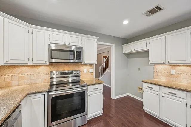 a kitchen with granite countertop white cabinets stainless steel appliances and wooden floor