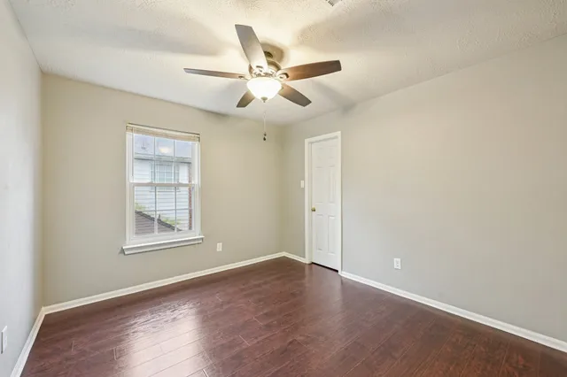 an empty room with wooden floor fan and windows