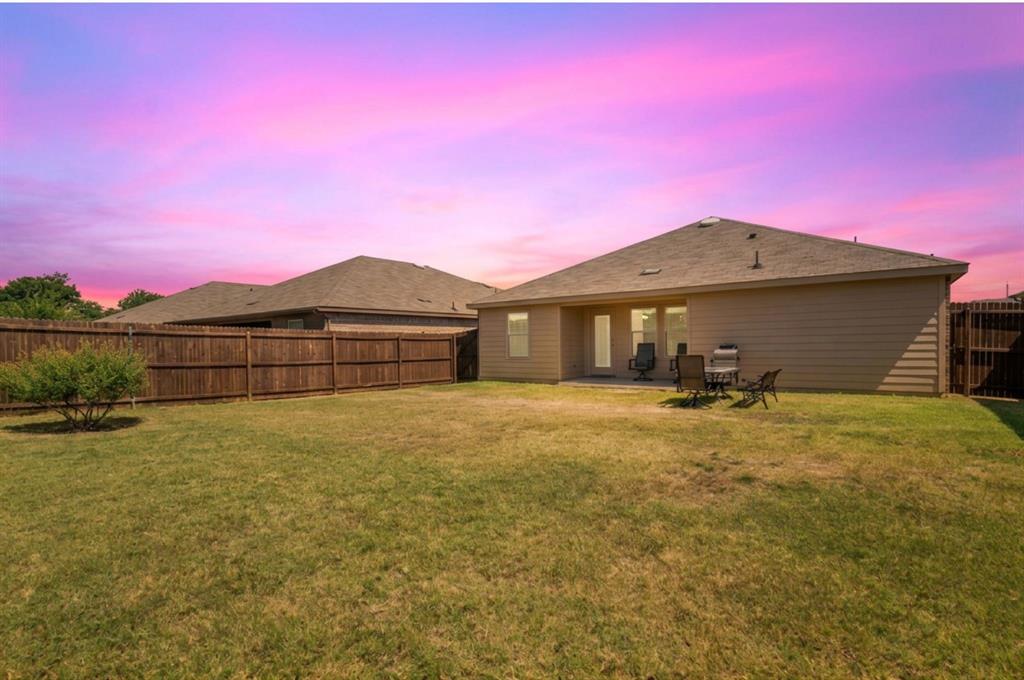 409 Wilson Way Denton, TX 76207 - Photo 31 of 33 Expansive green lawn featuring a privacy fence, a small planted bush, and a rear patio area