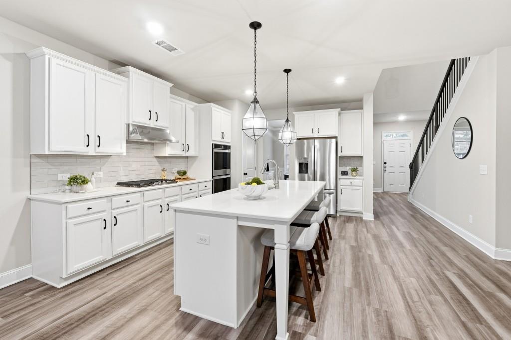 1849 Hanwoo Lane Powder Springs, GA 30127 - Photo 12 of 47 a kitchen with stainless steel appliances kitchen island granite countertop a wooden floor and white cabinets