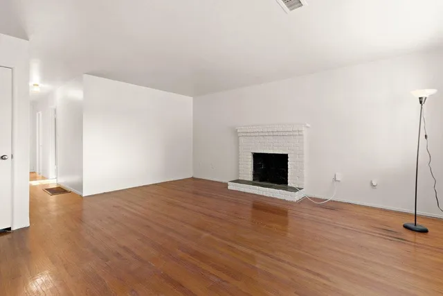 a view of an empty room with wooden floor and a fireplace