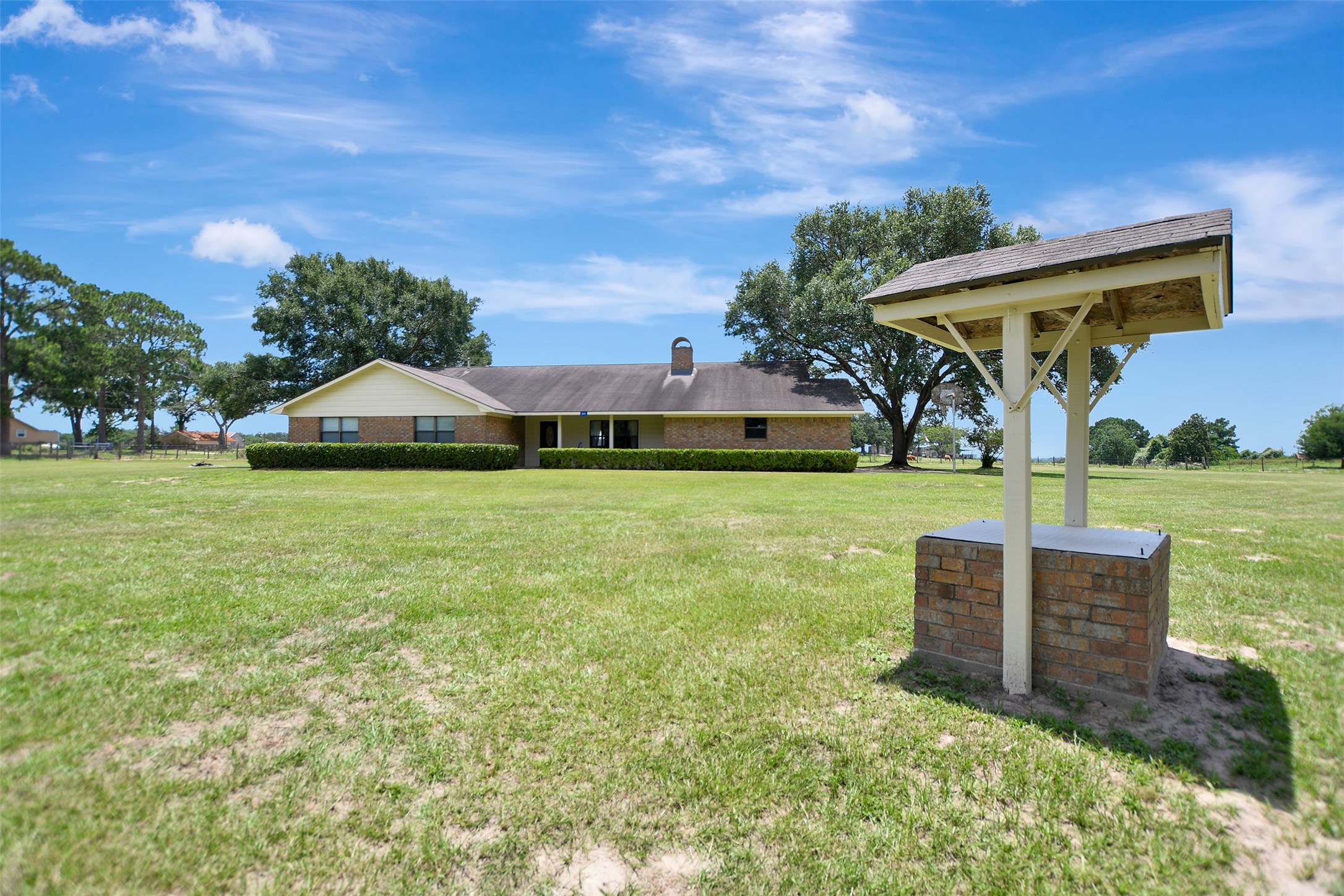 341 South S Loop Bellville, TX 77418 - Photo 4 of 33 A spacious single-story home sits on a large, open grassy lot, surrounded by mature trees. The property includes a well-maintained brick structure in the foreground, offering a serene country living environment.