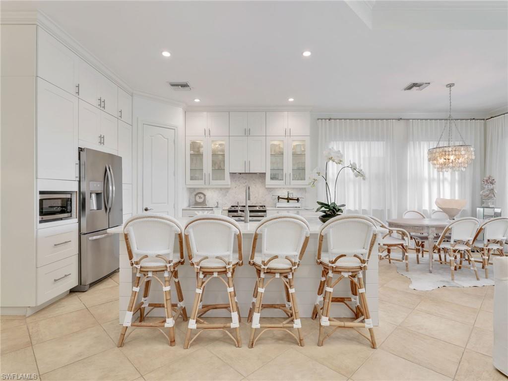1365 Serrano Circle Naples, FL 34105 - Photo 11 of 46 Kitchen with glass insert cabinets, decorative backsplash, ornamental molding, white cabinets, and a kitchen breakfast bar