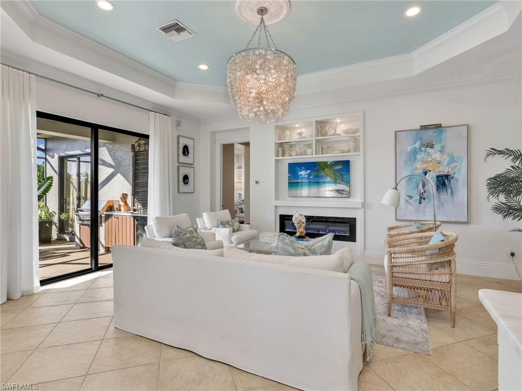 1365 Serrano Circle Naples, FL 34105 - Photo 17 of 46 Living room featuring a tray ceiling, a glass covered fireplace, crown molding, a chandelier, and recessed lighting
