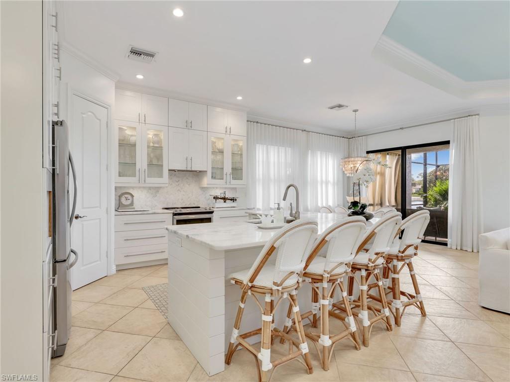 1365 Serrano Circle Naples, FL 34105 - Photo 9 of 46 Kitchen featuring glass insert cabinets, decorative light fixtures, backsplash, a breakfast bar area, and white cabinets
