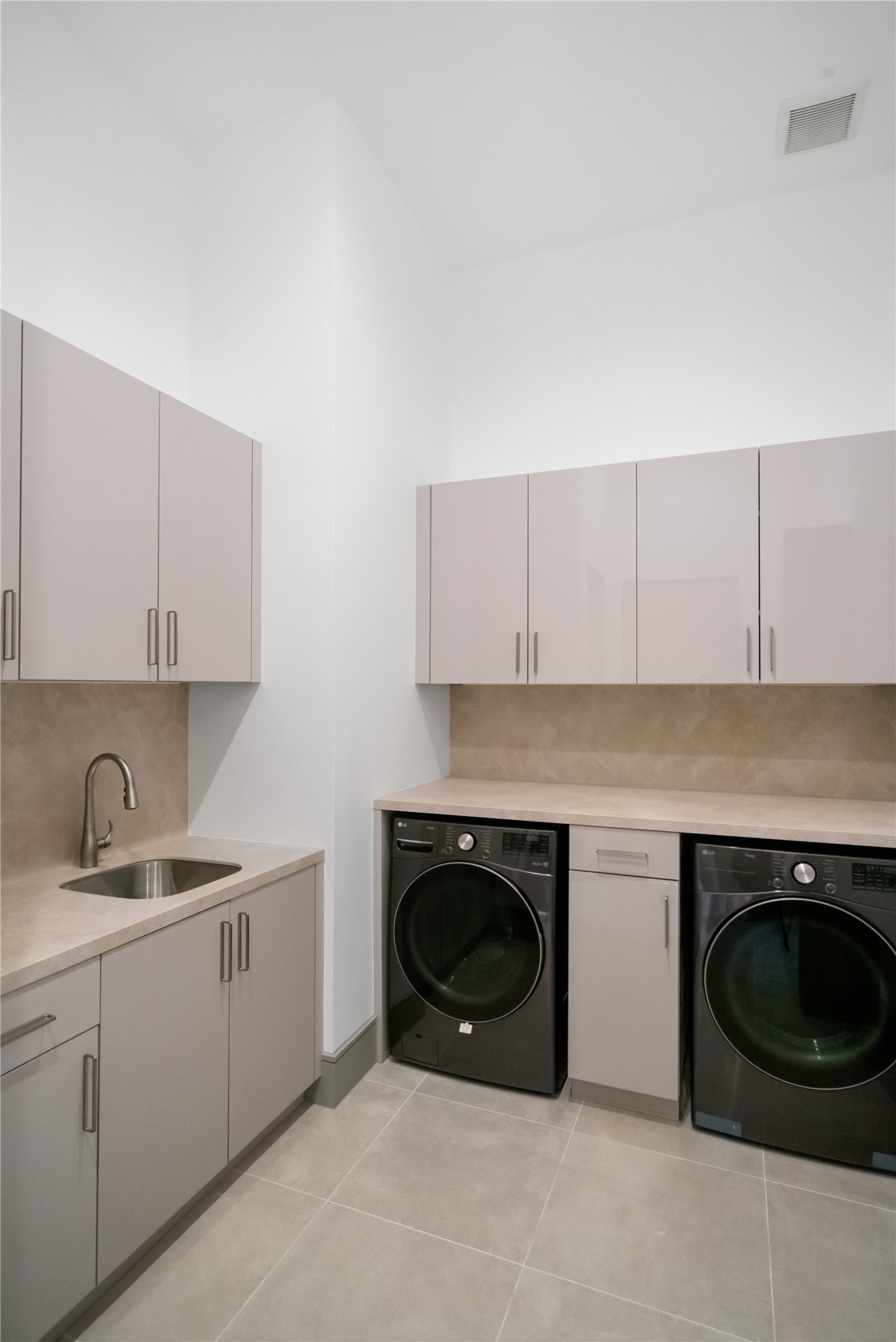47 Pronghorn Place Spring, TX 77389 - Photo 19 of 44 This photo shows a modern laundry room featuring sleek cabinetry, a built-in sink, and a washer and dryer set. The space is designed with neutral tones and ample storage, offering a functional and stylish utility area.