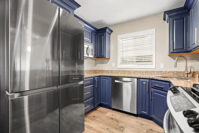 a kitchen with stainless steel appliances granite countertop a refrigerator a sink dishwasher a stove and a refrigerator with wooden floor