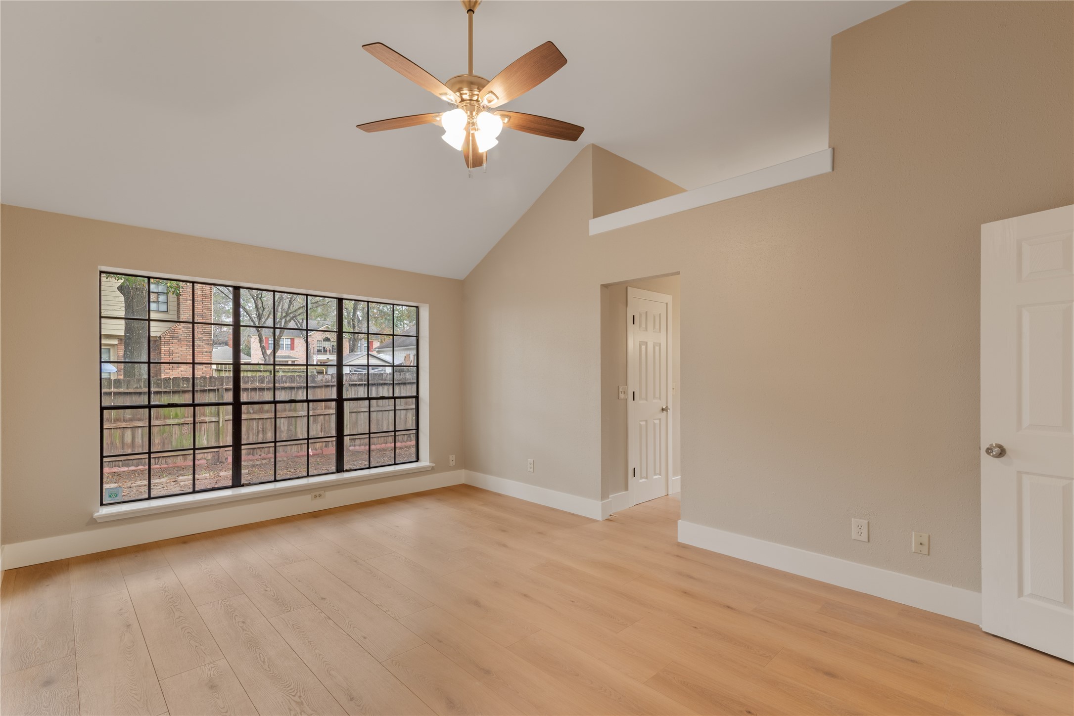 10 White Fawn Drive Spring, TX 77381 - Photo 20 of 25 This primary bedroom features a spacious, bright interior with high vaulted ceilings, a large window offering plenty of natural light, and light wood flooring. A ceiling fan adds a touch of elegance, and there's a door leading to an adjacent space, perfect for versatile use.
