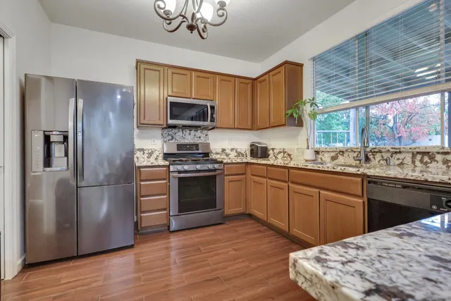 a kitchen with stainless steel appliances granite countertop a refrigerator a sink dishwasher a stove with wooden cabinets and floor