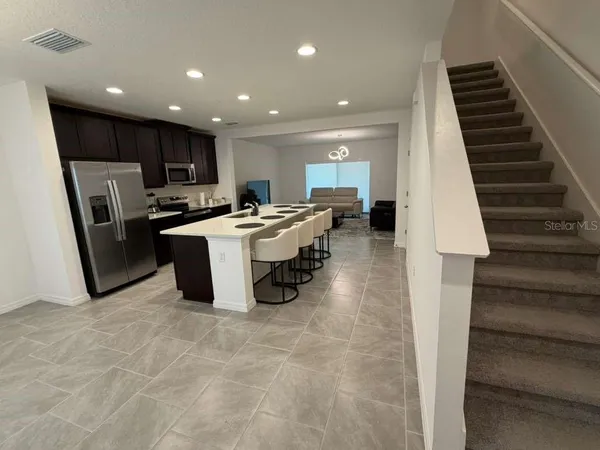 a living room with stainless steel appliances furniture a rug and a kitchen view